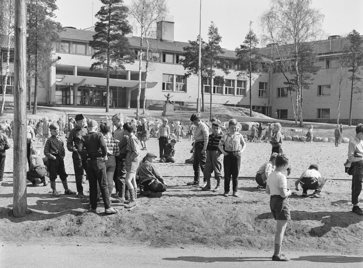 Lapsia koulun pihalla mustavalkoisessa valokuvassa.