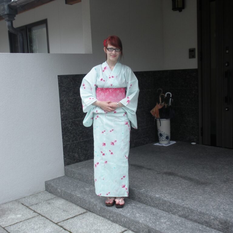 Nuori nainen seisoo talon portailla kimono päällään.